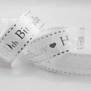 May include: White ribbon with silver text reading "60th Birthday" and "Happy Birthday". The ribbon features a heart symbol and a dotted border. Ideal for gift wrapping or party decorations.