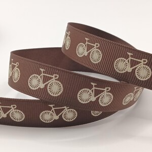 Könnte beinhalten: Ein braunes Ripsband mit einem sich wiederholenden Muster aus cremefarbenen Fahrrädern. Das Band hat eine texturierte, gerippte Oberfläche, auf der die Fahrradgrafiken in einer einheitlichen Ausrichtung entlang des Stoffes gedruckt sind.