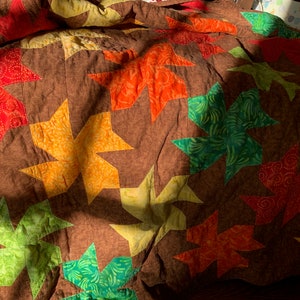 May include: A brown quilt with a patchwork design featuring multiple star-shaped fabric pieces in shades of red, orange, yellow, green, and brown.
