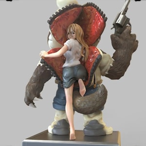 May include: A figurine of a woman with long blonde hair standing in front of a large, brown, furry creature with a red, open mouth. The creature is holding a gun in its right hand. The woman is wearing a white shirt and blue shorts.