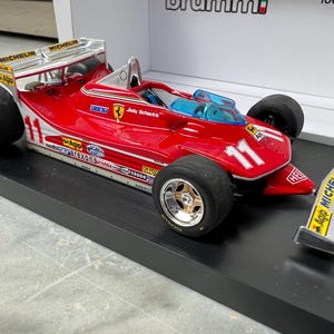 Puede incluir: Modelo de coche de carreras Ferrari de Fórmula 1 rojo y plateado, con el número 11. Tiene neumáticos negros, un alerón plateado y logotipos de patrocinadores. El modelo se exhibe sobre una base negra. Aproximadamente 20 cm de largo.