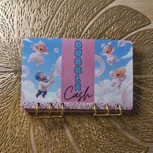 Peut inclure: Un organiseur d'enveloppes de trésorerie coloré avec un design fantaisiste. La couverture présente des personnages de dessins animés, des bulles et le texte "BUBBLE Cash". L'organisateur a des anneaux métalliques dorés.