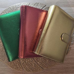 Può includere: Tre quaderni colorati e strutturati in verde, rosso e oro, disposti su un vassoio decorativo a forma di foglia. Ogni quaderno ha una chiusura a fibbia. I quaderni sono adatti per scrivere un diario o pianificare.