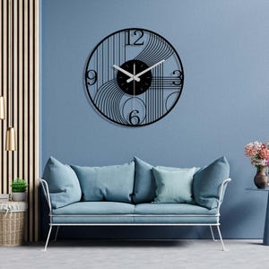 May include: A black and white geometric wall clock with a black background and white hands. The clock is hanging on a blue wall above a light blue sofa.