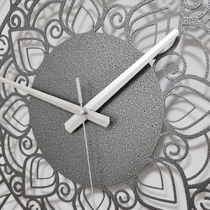 May include: A silver clock with a decorative mandala design around the edge. The clock face is gray with white hands.