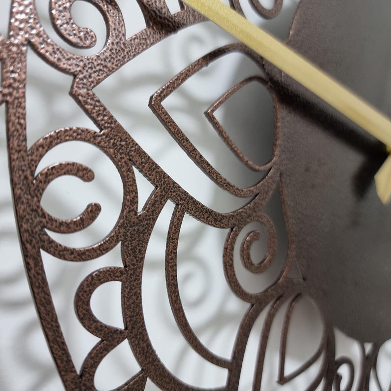 May include: Close-up of a copper-colored metal wall clock with a decorative, intricate, cut-out design. The clock has a gold-colored hand.
