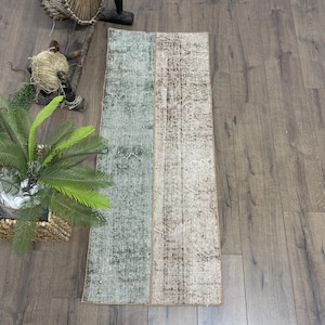 Puede incluir: Una alfombra de pasillo vintage con un esquema de color verde y beige. La alfombra está hecha de tejido tejido y tiene un aspecto desgastado.