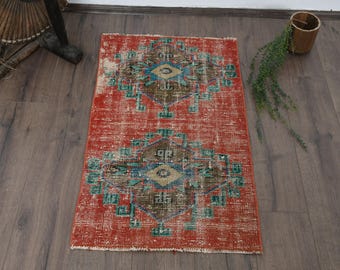 May include: A rectangular area rug featuring a vibrant red background with two symmetrical, diamond-shaped medallions in the center. The medallions incorporate intricate geometric patterns in shades of teal, brown, and beige, with a distressed finish.