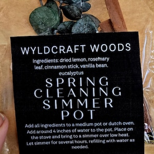 Könnte beinhalten: Eine braune Papiertüte mit einem Spring Cleaning Simmer Pot Kit. Das Kit enthält getrocknete Eukalyptusblätter, einen Zimtstange und ein schwarzes Etikett mit Anweisungen und dem Text "WYLDCRAFT WOODS".