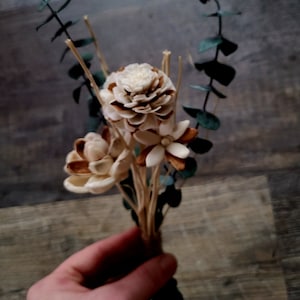Könnte beinhalten: Ein Strauß getrockneter Blumen mit weißen und braunen Blütenblättern und grünen Eukalyptusblättern.