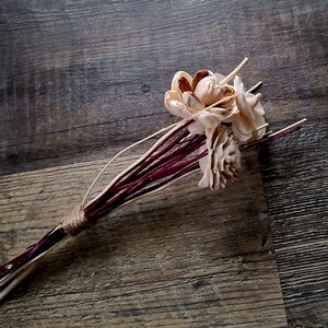 May include: A bouquet of dried flowers with white blossoms and burgundy stems tied together with twine.
