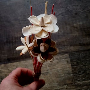 Könnte beinhalten: Ein Strauß aus Holzblumen mit roten Stielen. Die Blumen sind weiß und braun und mit Schnur zusammengebunden.