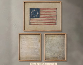 May include: Three framed prints on a light beige wall. The top print is a vintage American flag with 13 stripes and a circle of 13 stars. The two prints below are documents, one titled "We the People" and the other titled "In Congress, July 4, 1776". The text on the documents is difficult to read. The prints are all in wooden frames.