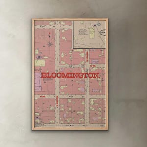 May include: A framed vintage map of Bloomington, Indiana, featuring a detailed street layout in shades of pink and beige. The word "BLOOMINGTON" is prominently displayed in red. A compass rose and street names are also visible.