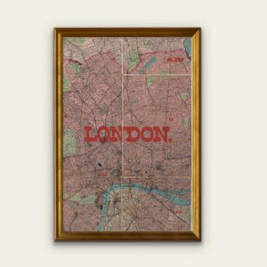 May include: A framed vintage map of London, featuring a detailed street layout in shades of pink, green, and brown. The word "LONDON" is prominently displayed in bold red letters across the map. The frame is a warm gold color.