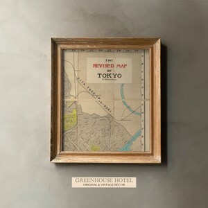 Puede incluir: Un mapa vintage enmarcado de Tokio, Jap&oacute;n, con el t&iacute;tulo "The Revised Map of Tokyo" en letras rojas. El mapa est&aacute; en un marco de madera claro y tiene un fondo marr&oacute;n claro. El mapa muestra las calles y v&iacute;as fluviales de la ciudad. El texto "GREENHOUSE HOTEL ORIGINAL & VINTAGE DECOR" est&aacute; impreso debajo del marco.