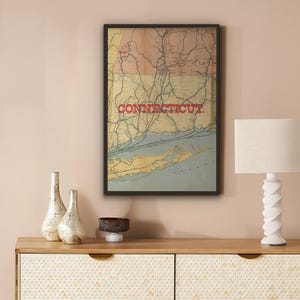 Peut inclure: Une carte vintage encadrée du Connecticut, avec une représentation détaillée de la géographie de l'État. Le mot "CONNECTICUT" est affiché en rouge sur la carte. La carte est encadrée de noir.