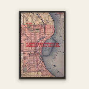 May include: Framed vintage map of Milwaukee, Wisconsin, featuring a detailed street grid in shades of pink and tan. The city's name is boldly overlaid in red. The map includes the lakefront and river systems, all within a black frame.