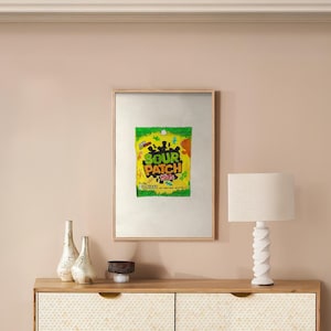 May include: A framed print of a Sour Patch Kids candy bag. The bag is yellow with green and black accents. The text "Sour Patch Kids" is in black letters on the bag.