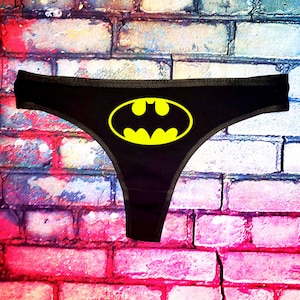 Könnte beinhalten: Schwarze Spitzenunterwäsche mit einem gelben Batman-Logo.