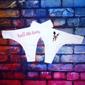 May include: White lace underwear with the text "Roll Me Over" in pink lettering. The underwear has a pink ribbon and a spoon and fork design.