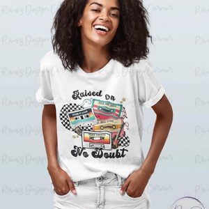 Puede incluir: Camiseta blanca con un dise&ntilde;o retro con cintas de cassette y el texto "Raised on No Doubt". El gr&aacute;fico incluye un patr&oacute;n de cuadros y estrellas. Un art&iacute;culo casual para el uso diario.
