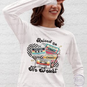 Puede incluir: Camiseta blanca de manga larga con un dise&ntilde;o retro con cintas de cassette y el texto "Raised On No Doubt". El dise&ntilde;o incluye un coraz&oacute;n a cuadros, estrellas y una guitarra, evocando un tema musical vintage.