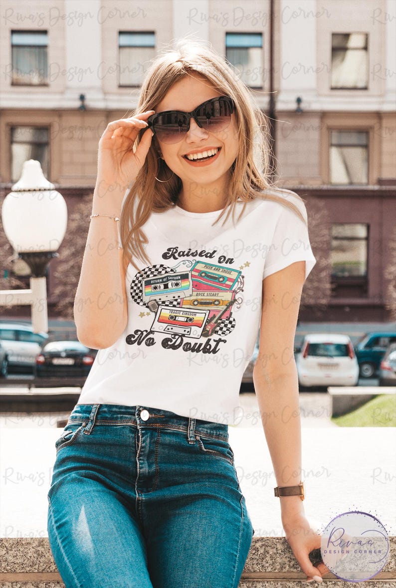 Puede incluir: Camiseta blanca con un dise&ntilde;o retro de casete y el texto "Raised On No Doubt". La persona lleva vaqueros azules y gafas de sol. El tema es la m&uacute;sica vintage.
