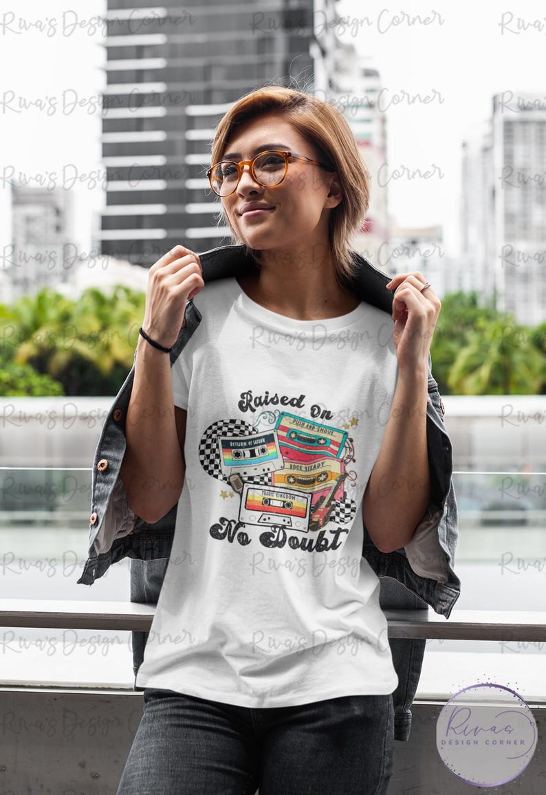 Puede incluir: Camiseta blanca con un dise&ntilde;o retro de casete y el texto "Raised On No Doubt". El dise&ntilde;o presenta cintas de casete coloridas y un fondo a cuadros. La persona lleva gafas y una chaqueta negra.