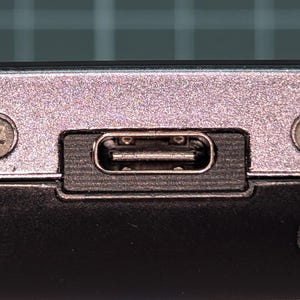 May include: Close-up of a device's port panel. The panel is silver with a USB-C port, two screws, and a headphone jack. The USB-C port is rectangular and black. The screws are silver and have a cross-shaped head.