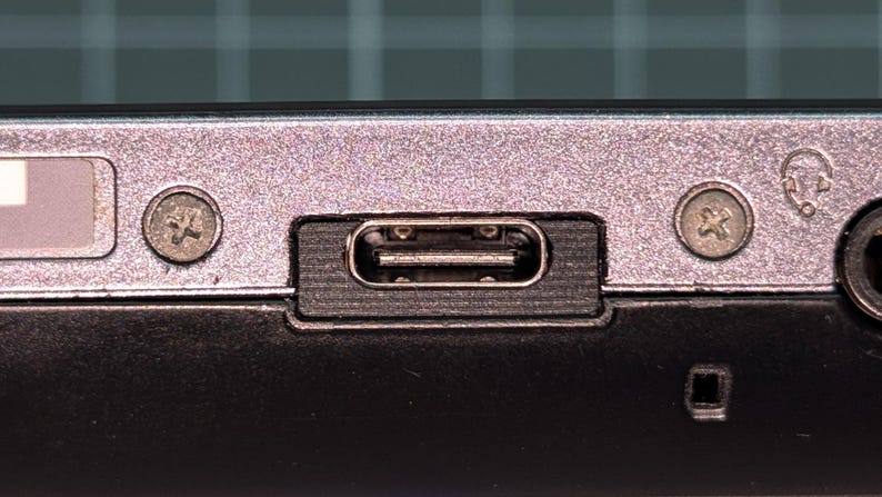 May include: Close-up of a device's port panel. The panel is silver with a USB-C port, two screws, and a headphone jack. The USB-C port is rectangular and black. The screws are silver and have a cross-shaped head.