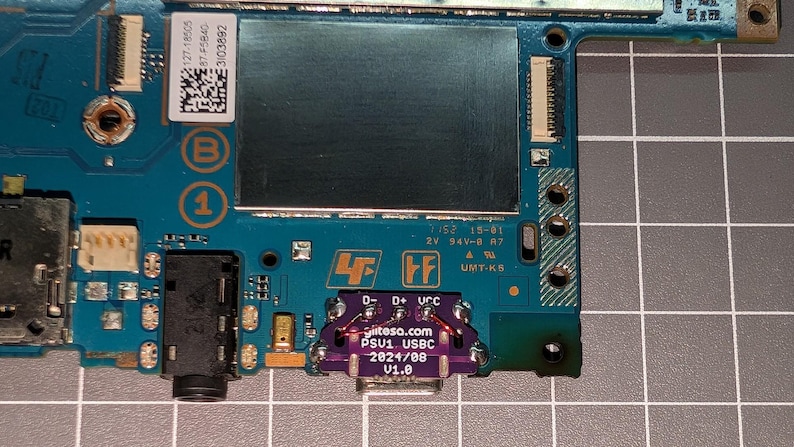 May include: A close-up of a circuit board with various electronic components. The board is primarily teal and green, with a purple USB-C port. Text on the board includes "tesa.com PSU1 USBC 2024/08 V1.0".