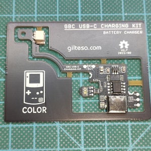 以下が含まれることがあります： 「GBC USB-C CHARGING KIT」と「giltesa.com」の文字が入った黒色のGBC USB-C充電キット。バッテリーチャージャーとゲームボーイカラーの図が含まれています。