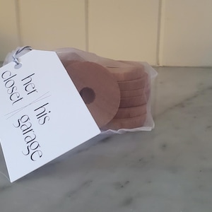 May include: A white tag with the text "her closet his garage" attached to a bag of brown, round, fabric discs.
