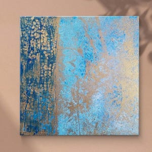 Può includere: Dipinto astratto quadrato con superficie strutturata. L'opera presenta una combinazione di tonalità blu e oro, con una sezione verticale di oro strutturato sul lato sinistro e uno sfondo azzurro e oro.