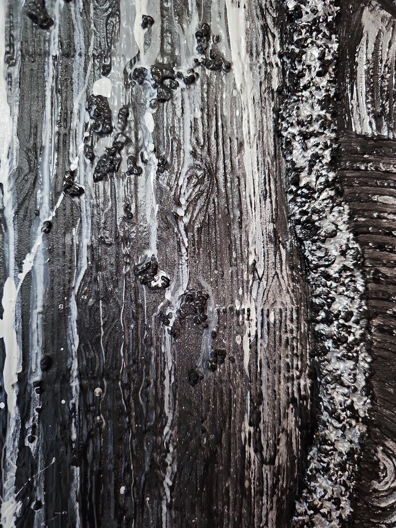 May include: Abstract art piece with a textured surface. The artwork features a combination of black, white, and gray tones. Dripping white paint and small black textured elements are visible, creating a dynamic visual effect. The piece has a rough, tactile quality.