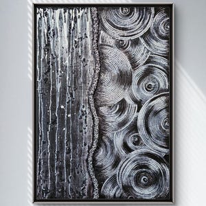 May include: Abstract black and white painting in a black frame. The artwork features a textured, vertical section with white drips and splatters, and a section of swirling, concentric circles. A textured line divides the two sections.
