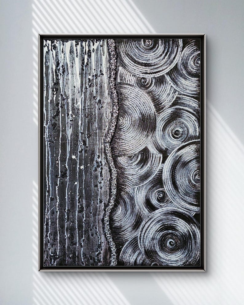 May include: Abstract black and white painting in a black frame. The artwork features a textured, vertical section with white drips and splatters, and a section of swirling, concentric circles. A textured line divides the two sections.