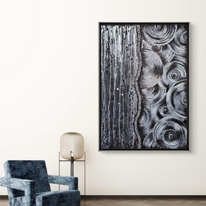 May include: Abstract black and white artwork in a black frame. The painting features a vertical section with white drips and a textured side with concentric circles. A blue velvet armchair and a lamp are in the foreground.