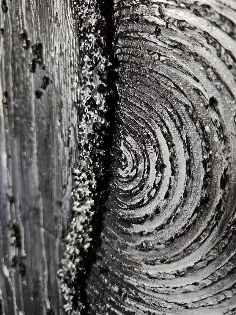 May include: Close-up of a textured abstract artwork in shades of gray and black. The piece features a swirling pattern on the right, a rough, granular texture in the center, and a vertical, wood-grain-like texture on the left. The artwork has a three-dimensional appearance.