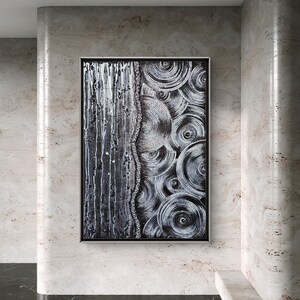 May include: Abstract black and white artwork in a silver frame. The painting features a textured design with vertical lines on the left and concentric circles on the right. The artwork is displayed on a wall with a marble-like texture.