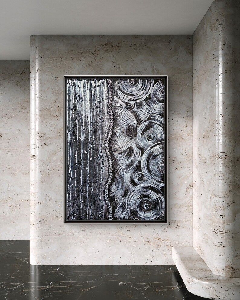 May include: Abstract black and white artwork in a silver frame. The painting features a textured design with vertical lines on the left and concentric circles on the right. The artwork is displayed on a wall with a marble-like texture.