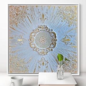 Può includere: Opera d'arte incorniciata con sfondo azzurro chiaro e dettagli dorati ornati. Il disegno centrale è un medaglione circolare con motivi intricati. Una tazza bianca e un libro sono in primo piano.