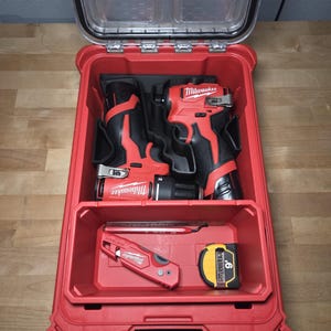 May include: Red and black power tools and accessories are organized inside a red toolbox with a clear lid. The toolbox contains two drills, a utility knife, and a 9-foot tape measure.