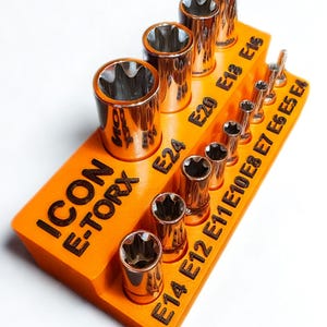 May include: An orange tool organizer with the text "ICON E-TORX" and various sizes of E-Torx sockets. The sockets are arranged in rows and are made of a shiny, metallic material. The sizes are labeled on the organizer.
