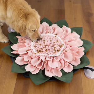 Könnte beinhalten: Eine rosa blütenförmige Hunde-Futtermatte mit grünen Blättern und einer dunkelgrauen Basis. Die Mitte der Blume enthält Hundefutter. Ein Golden Retriever wird beim Fressen von der Matte gezeigt.
