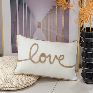 May include: A white rectangular pillow with a brown rope design spelling out the word "love".