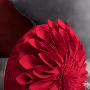 May include: Red round throw pillow with a flower design. The pillow is made of a soft, plush fabric and has a 3D effect.