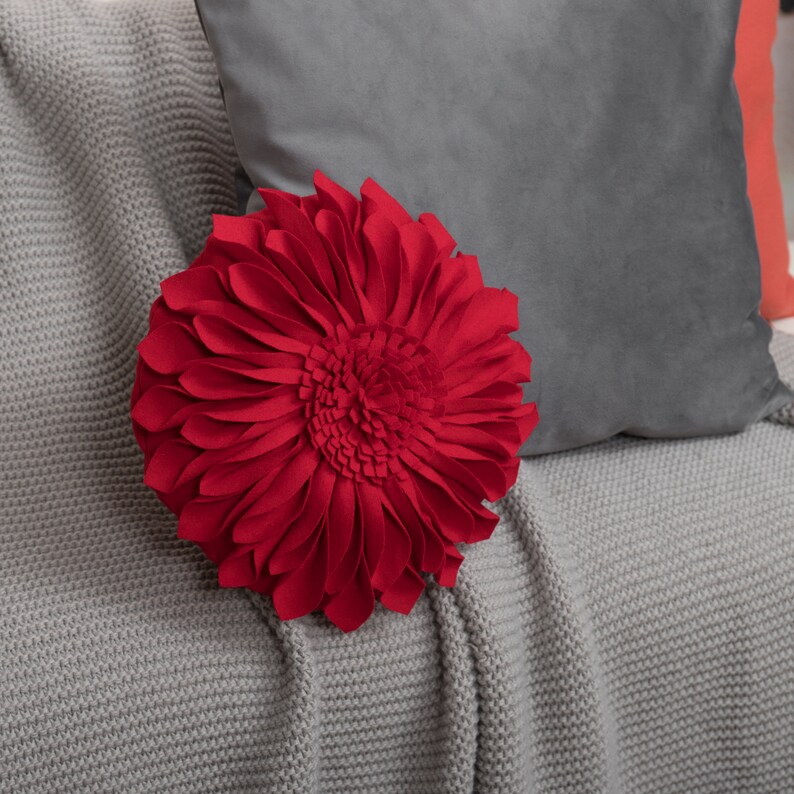 May include: A red felt flower pillow with a gray knitted throw blanket.