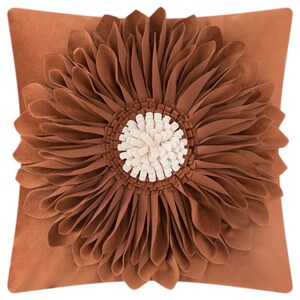 May include: A brown throw pillow with a large, brown, 3D flower design. The flower has a white centre.